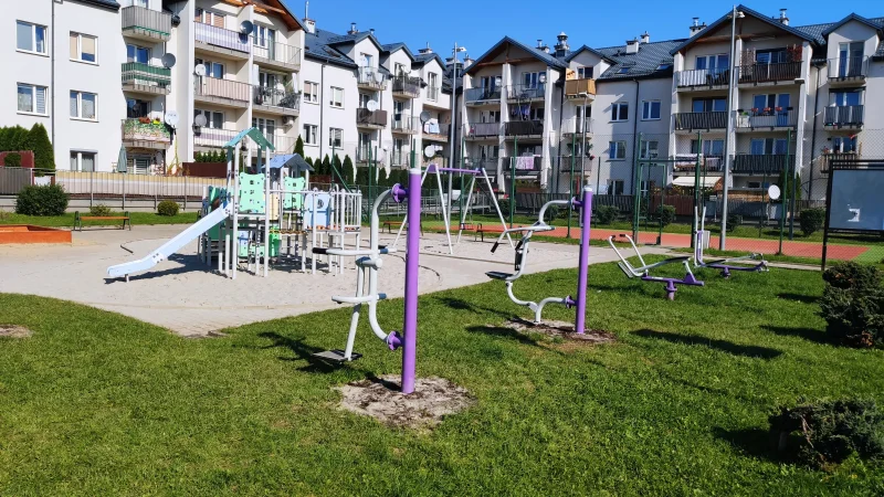 Nowoczesny plac zabaw w Nowym Sączu z elementami do zabawy dla dzieci i urządzeniami sportowymi na świeżym powietrzu.