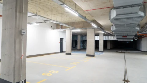 Puste i nowoczesne wnętrze podziemnego parkingu z betonowymi kolumnami nośnymi oraz oświetleniem na szynach.