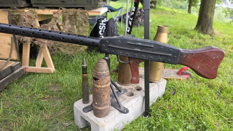 Zbliżenie na historyczny karabin wojskowy wystawiony na trawie; broń ma ciemne drewno i metalowe elementy, sugerując użycie w czasie II wojny światowej.