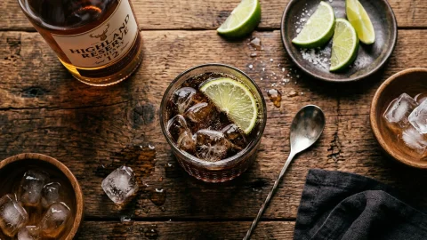 Szklanka whisky z limonką i plasterkami cytryny, podana na drewnianej desce z lodem.