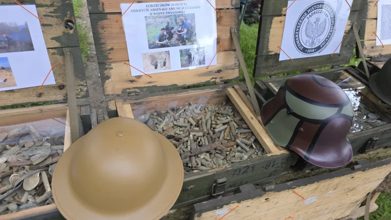 Zbliżenie na historyczny zestaw militariów w skrzyniach; widoczne są elementy wyposażenia wojskowego, takie jak hełm i amunicja z okresu II wojny światowej.