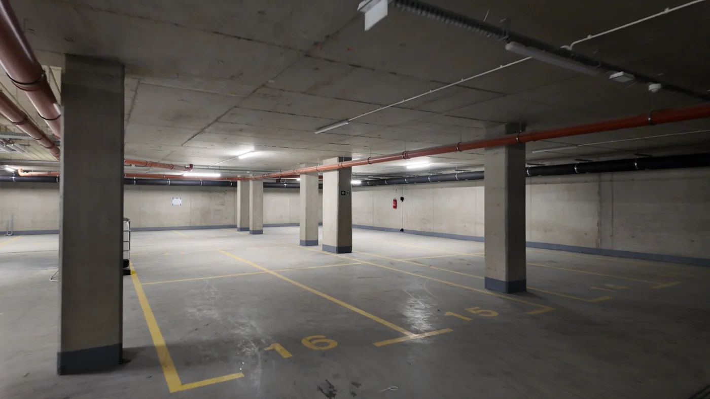 Pusty i surowo wykończony budowlany hol lub parking podziemny z widocznymi betonowymi słupami nośnymi i instalacjami
