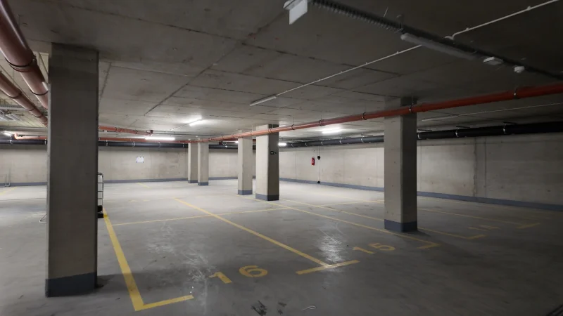 Pusty i surowo wykończony budowlany hol lub parking podziemny z widocznymi betonowymi słupami nośnymi i instalacjami