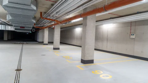 Puste miejsce parkingowe w nowoczesnym garażu podziemnym z widocznymi instalacjami wentylacyjnymi i rurami