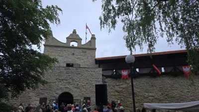 Kamienne mury baszty Kowalskiej w Nowym Sączu, widok na historyczną architekturę obronną otoczoną zielenią drzew.