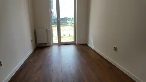 Puste wnętrze z nowym drewnianym panelem podłogowym i białymi ścianami, gotowe do urządzania.