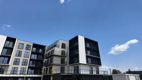 Nowoczesny kompleks mieszkalny z wielopiętrowymi budynkami o czystej architekturze, usytuowany na tle niebieskiego nieba.